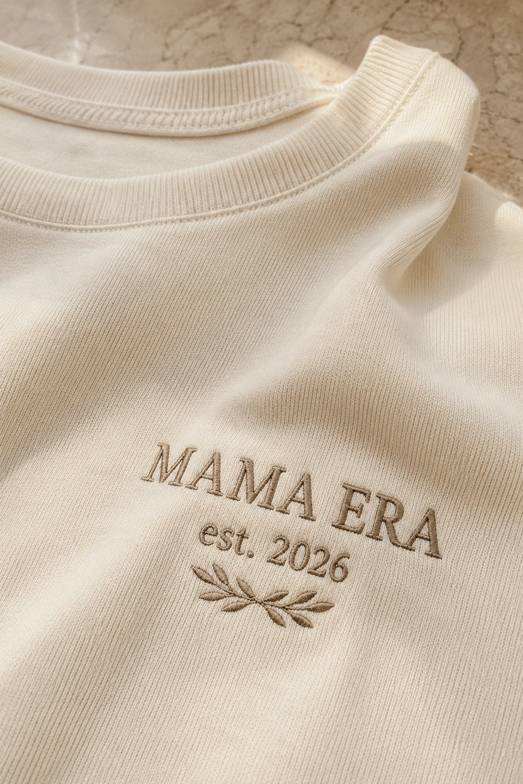 Close-up of tonal Mama Era embroidery on warm ivory fabric